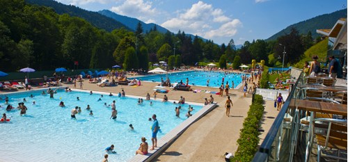 View of two outdoor swimming pools full of people, surrounded by trees and mountains