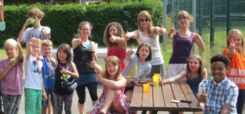 A group of children sitting at a bench outside smiling and cheering